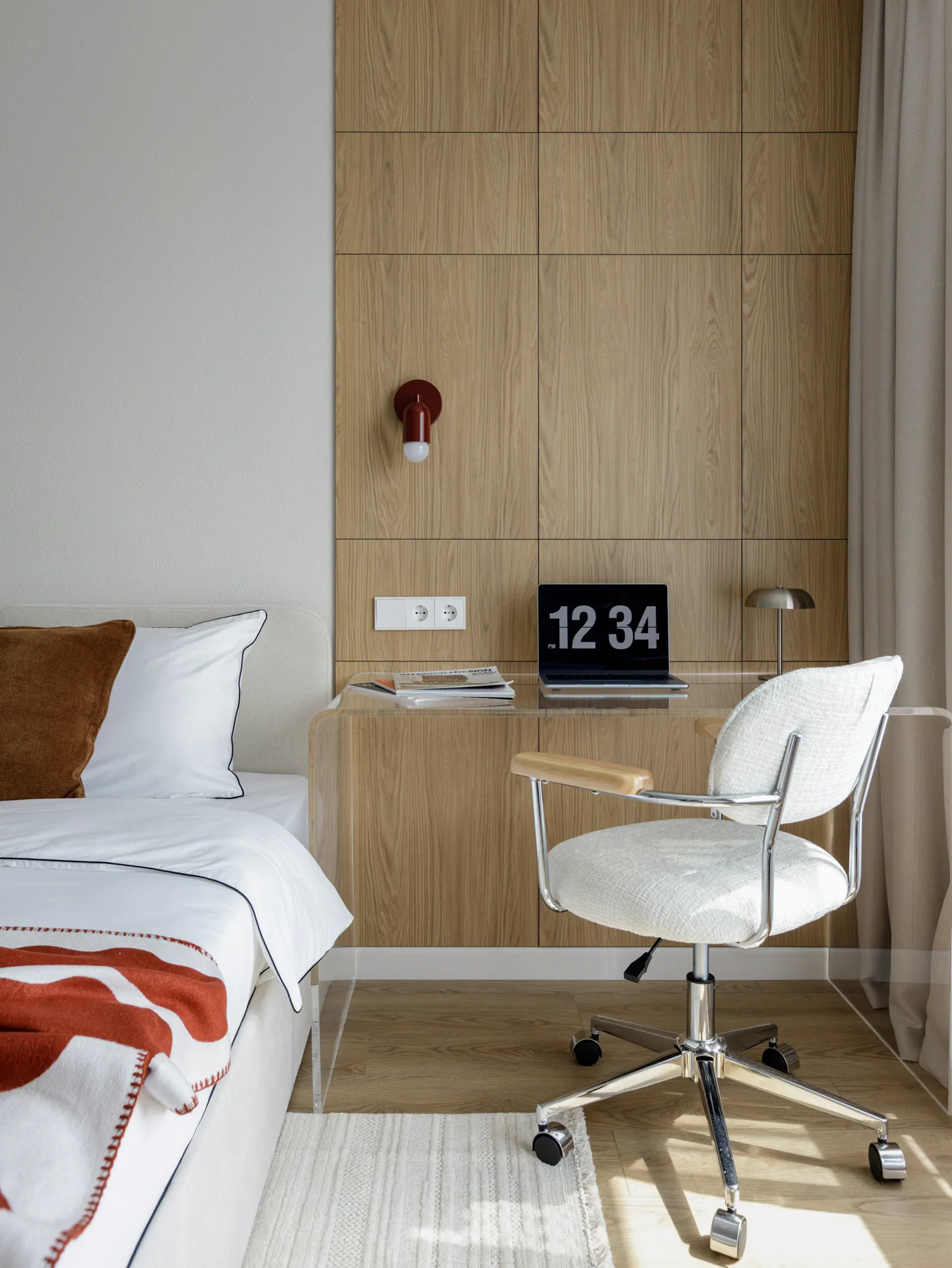 Quarto claro com cama arrumada, mesa de madeira, cadeira branca e luminária de parede.